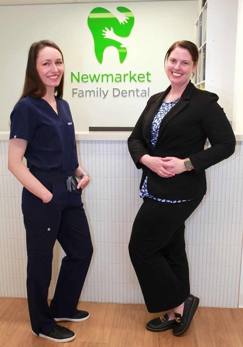 Dr Emily Shorten and Nikki standing in front of the Newmarket Family Dental reception desk and logo